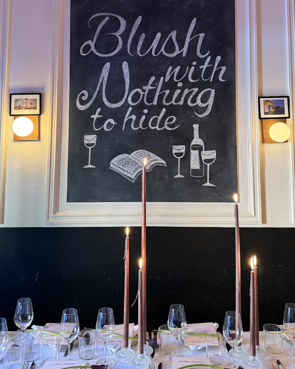 Chalkboard mural saying 'Brush with Nothing to hide' with wine glasses, a bottle, and an open book illustration over a candlelit dining setup.