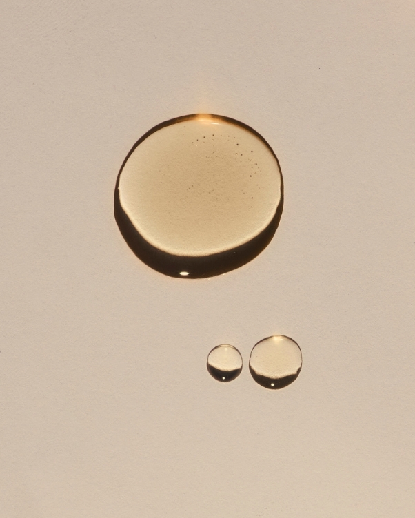 Three amber liquid droplets on a pale surface: one large circle above two smaller circles.