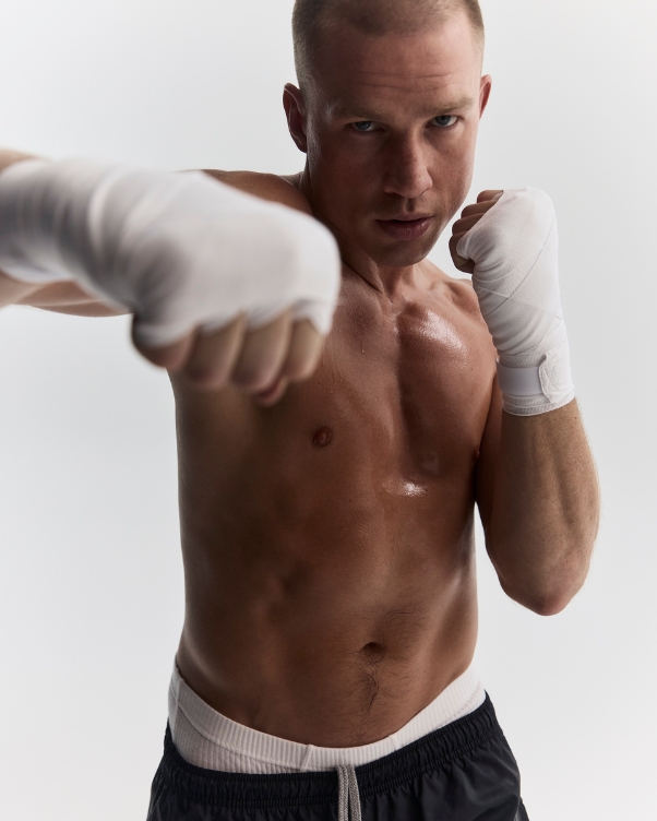 Male boxer with white hand wraps and black shorts, shirtless, in a fighting stance toward the camera.
