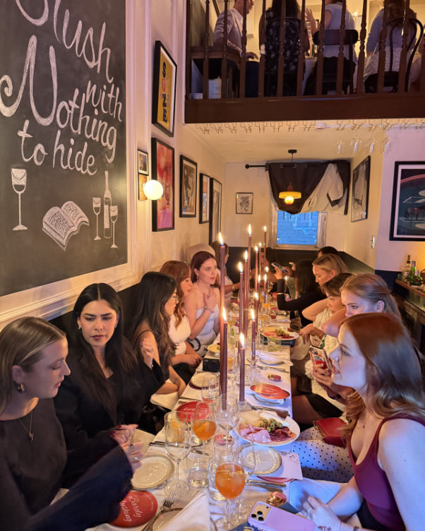 Group of friends having a candlelit dinner at a long communal table in a cozy restaurant.