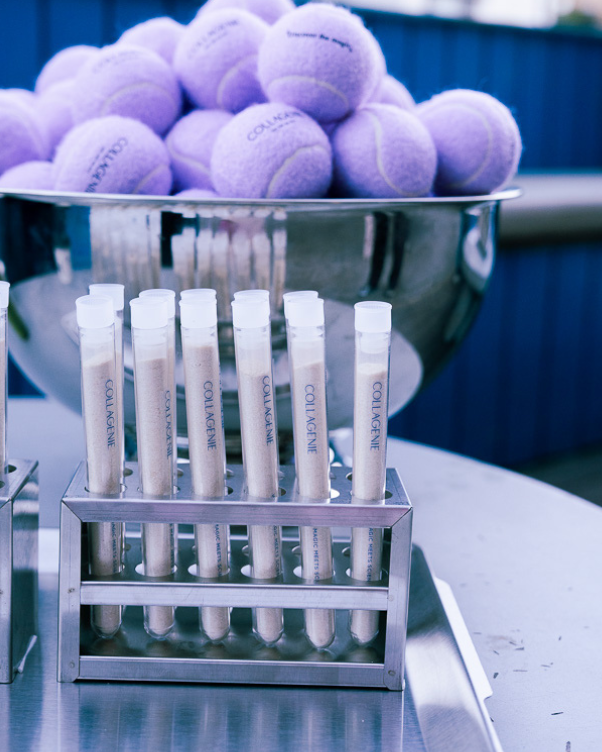 Rack of clear test tubes labeled 'COLLAGEN' in a metal holder on a lab bench, with a large bowl of purple tennis balls in the background.