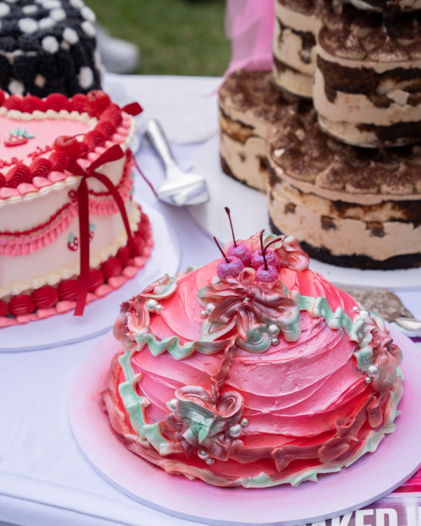 Pink frosted cake with green and pink swirls and cherries on top, on a party table outdoors.