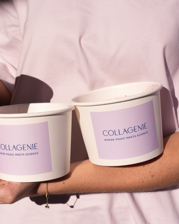Two white cups with lavender Collagenie labels are held in an arm wearing a pink shirt, sunlit.