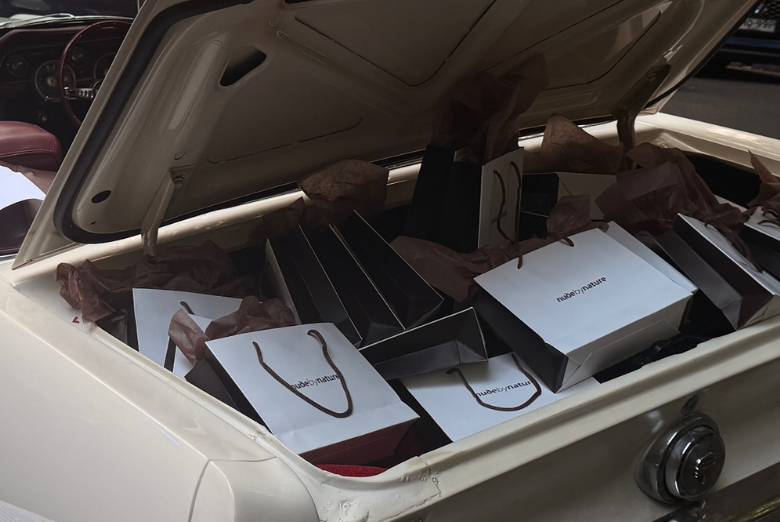 Open car trunk filled with white and brown shopping bags and tissue paper, suggesting a shopping trip or gift haul.