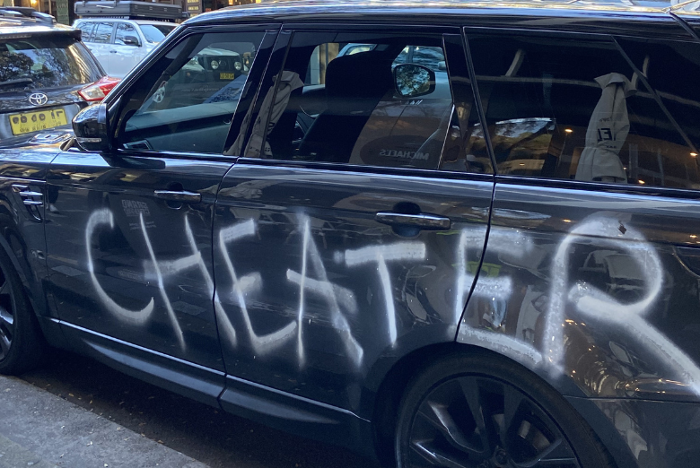 Black SUV with large white graffiti spray-painted across its side on the street.