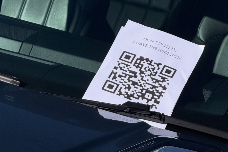 Sheet of paper with a large QR code and the caption 'DON'T DENY IT. I HAVE THE RECEIPTS!' resting on a car dashboard behind the windshield.