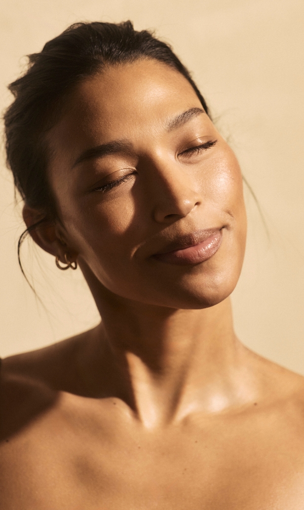 Close-up of a woman with eyes closed, calm expression, bathed in warm sunlight.