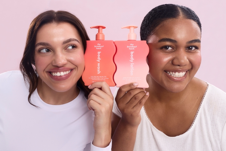 Two women smiling and holding pink bottles labeled body wash and lotion for a product demo.