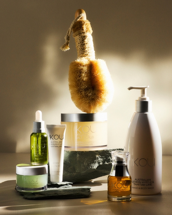 Assorted skincare products arranged on a stone platform with a large natural body brush upright in the center.